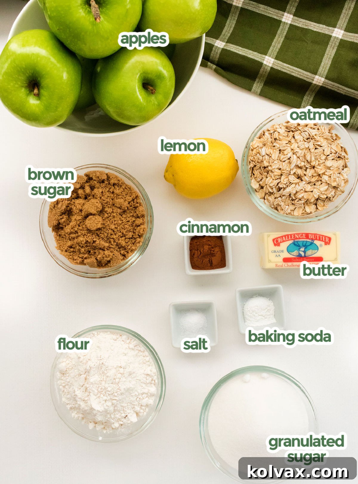 A spread of all the ingredients needed to make Apple Crisp, including apples, rolled oats, a lemon, brown sugar, cinnamon sticks and ground cinnamon, butter, baking soda, salt, all-purpose flour, and granulated sugar.