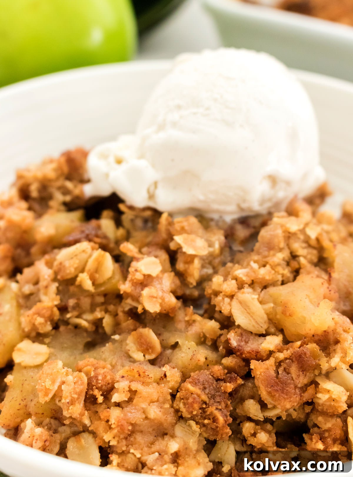 A pristine white bowl brimming with warm Apple Crisp, lovingly adorned with a single scoop of creamy vanilla ice cream, ready to be enjoyed.