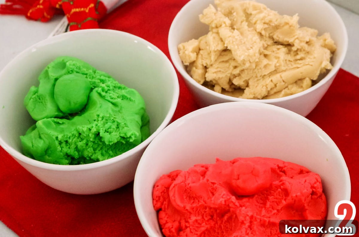 Three separate white bowls, each containing a perfectly tinted portion of sugar cookie dough: one vibrant red, one festive green, and one pristine white, ready for marbling.