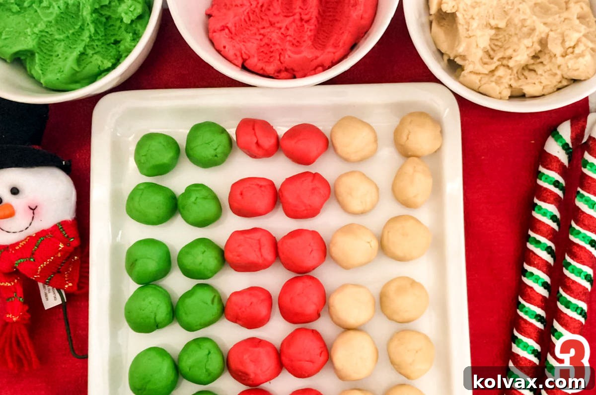A large white serving platter neatly covered with rows of small, perfectly rounded sugar cookie dough balls in alternating vibrant green, festive red, and pure white colors.