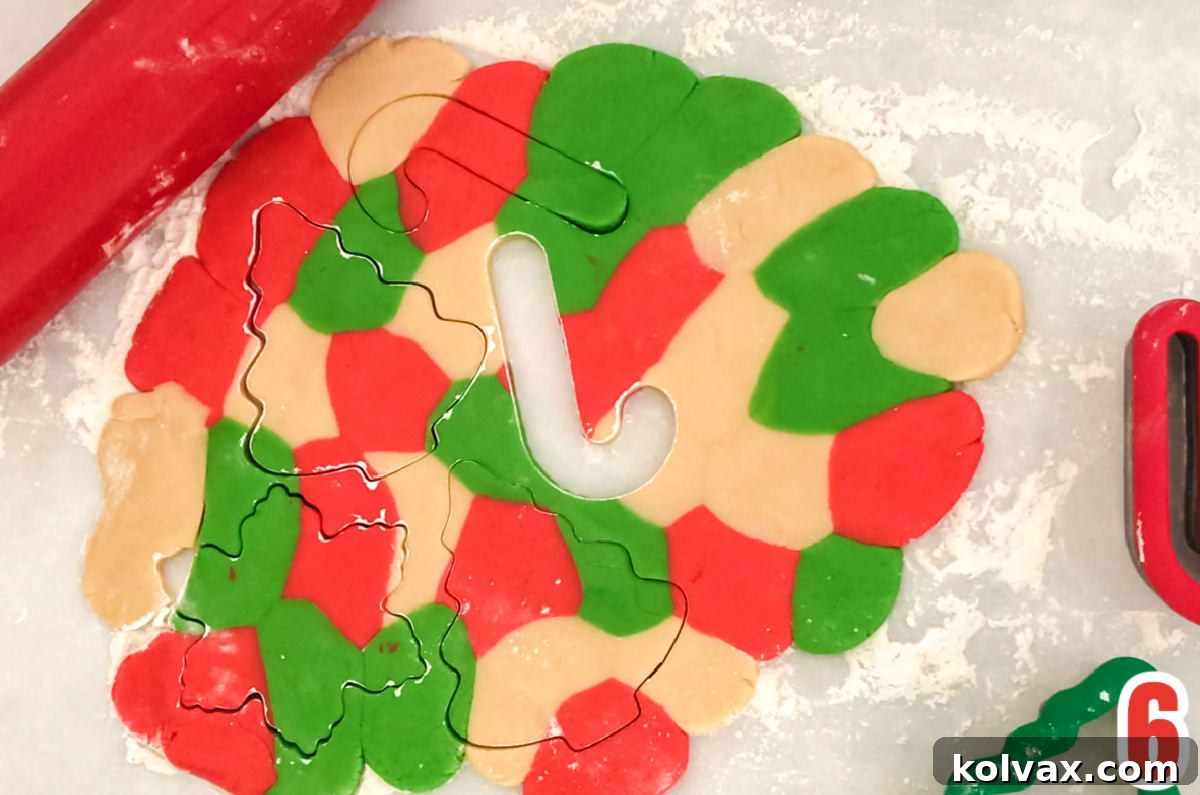 An overhead shot of vibrantly marbled sugar cookie dough rolled out on a flat surface, accompanied by a rolling pin and an assortment of festive Christmas cookie cutters, poised for baking.