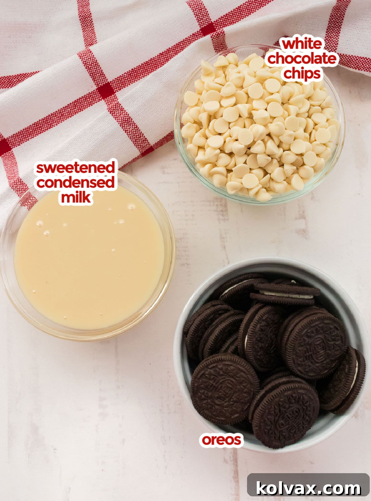 All the essential ingredients neatly arranged for making Oreo Fudge, including two bags of glistening White Chocolate Chips, a can of creamy Sweetened Condensed Milk, and a stack of classic Oreo Cookies, ready to be transformed into a delectable treat.