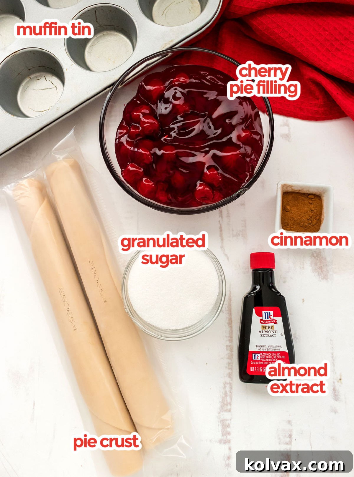 Bite-Sized Cherry Delights 3 A flat lay showing all the essential ingredients for making Mini Cherry Pies: two cans of cherry pie filling, a bowl of granulated sugar, a bottle of cinnamon, a bottle of almond extract, and a package of pre-made pie crusts.