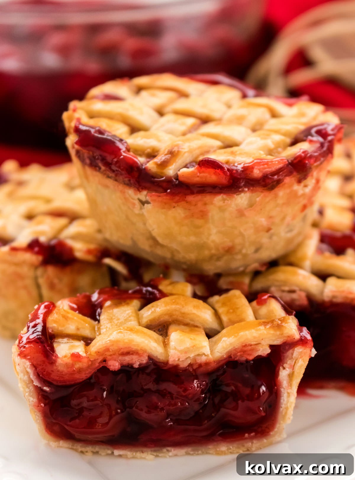 Bite-Sized Cherry Delights 7 A beautiful close-up of a stack of Mini Cherry Pies on a white plate. One pie is cut in half, revealing the luscious, ruby-red cherry filling nestled within the flaky golden crust. The image captures the inviting texture and irresistible appeal of the finished dessert.