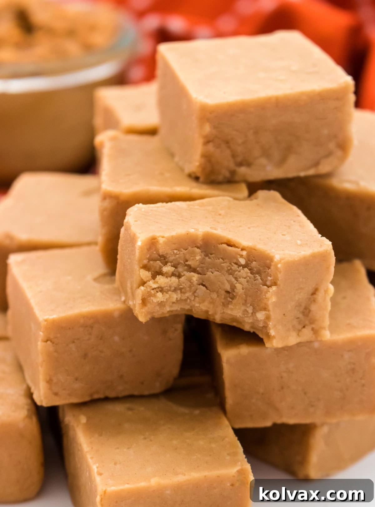 An enticing close-up of a stack of Easy Peanut Butter Fudge, with one piece showing a satisfying bite taken out, revealing its smooth and creamy interior.