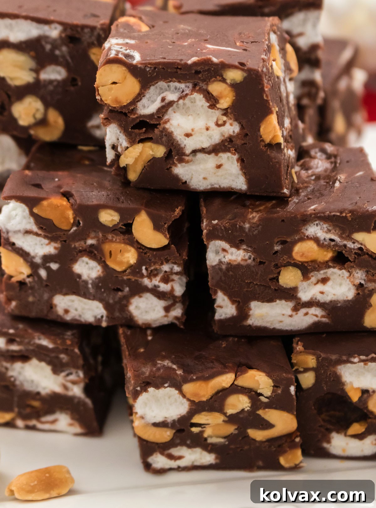 Decadent Rocky Road Bliss 8 A tempting closeup of several pieces of homemade Rocky Road Fudge, artfully stacked on a white serving platter, highlighting the rich chocolate, visible peanuts, and soft mini marshmallows within each decadent square.