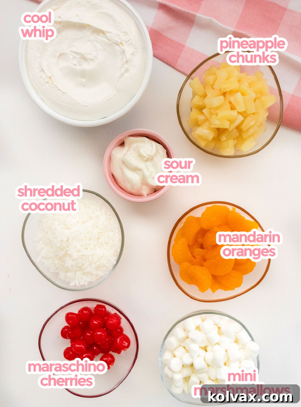 All the essential ingredients for Ambrosia Salad laid out: Cool Whip, canned pineapple chunks, sour cream, shredded coconut, canned mandarin oranges, maraschino cherries, and mini marshmallows.
