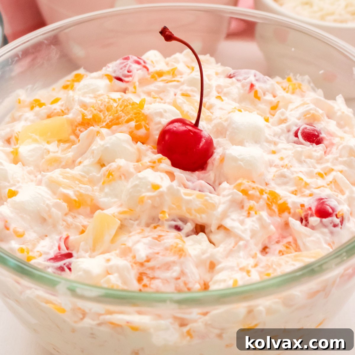 A stunning glass bowl overflowing with classic Ambrosia Salad, showcasing its creamy texture, colorful fruits, and fluffy marshmallows, topped with a bright maraschino cherry.