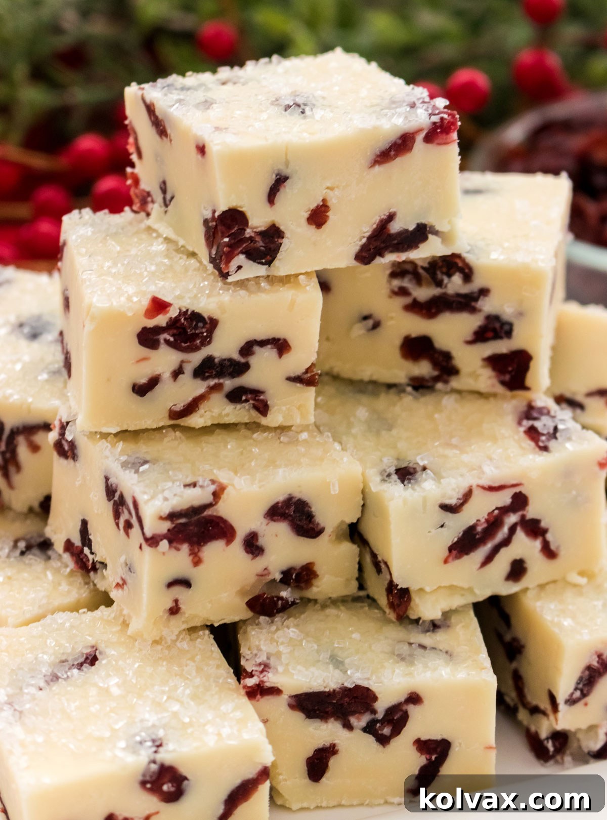 Close up on a stack of White Chocolate Cranberry Fudge sitting on a white serving platters in front of Christmas greenery.