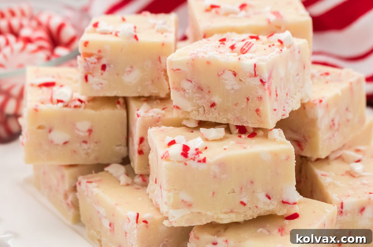 Closeup on a stack of Peppermint Fudge candies sitting on a white plate with a glass bowl filled with Peppermint Candies in the background.