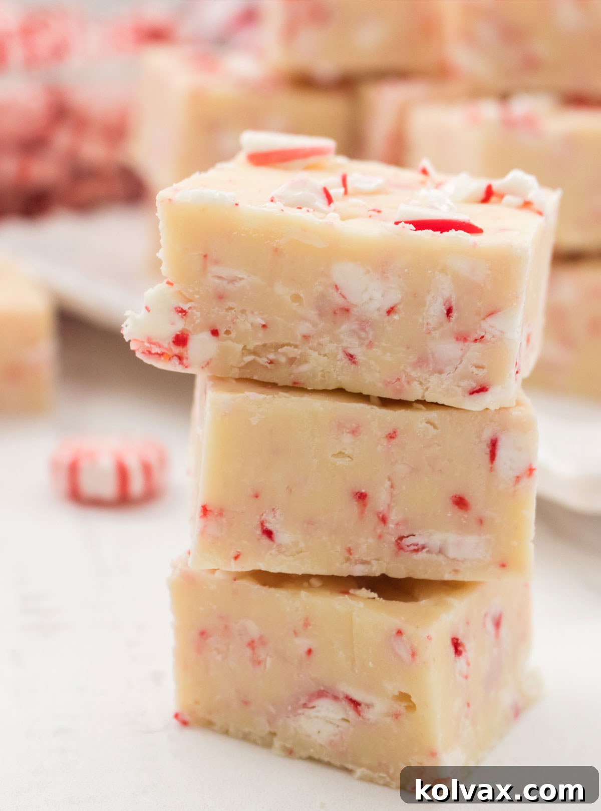 Closeup on a stack of three Peppermint Fudge candies sitting on a white table in front of a serving platter filled with Peppermint Fudge.
