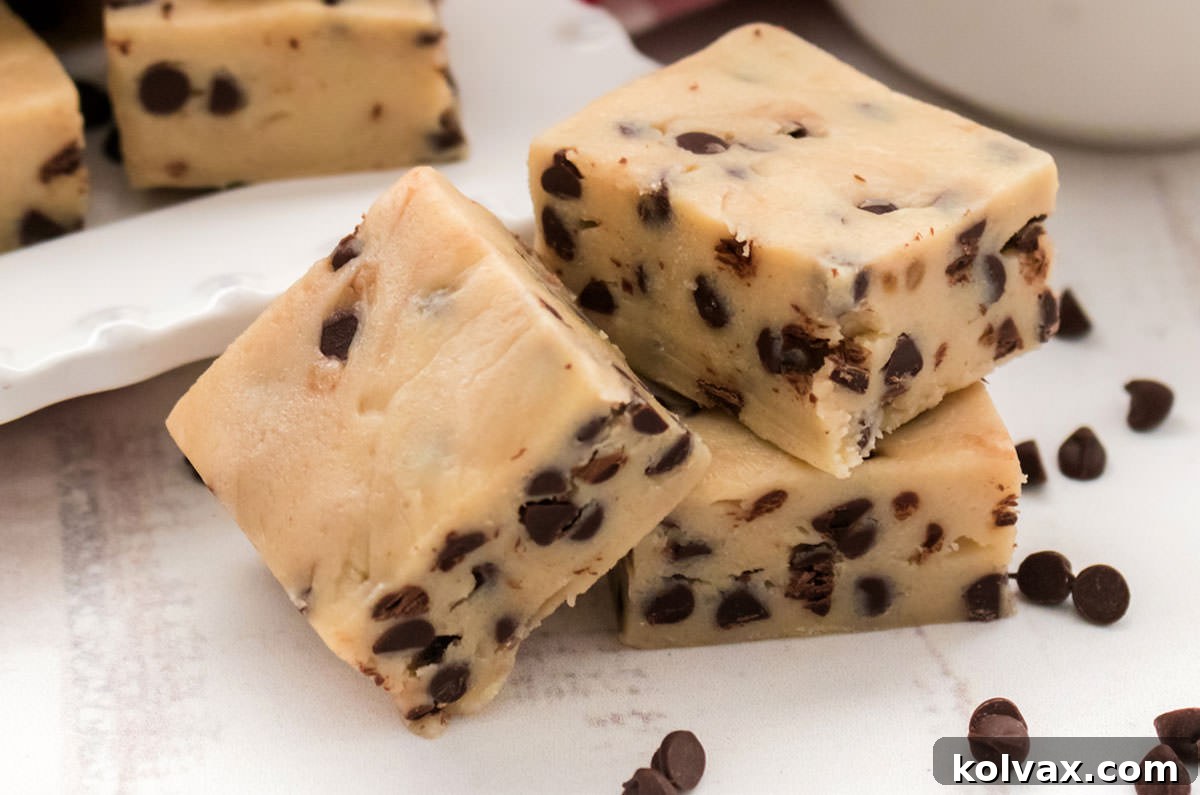 Three pieces of rich Cookie Dough Fudge, sprinkled with mini chocolate chips, rest on a pristine white surface.