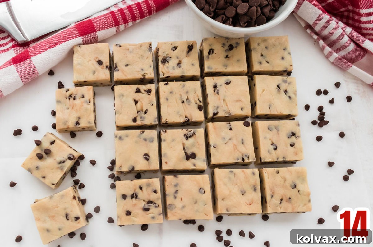 An overhead shot showcasing numerous perfectly cut squares of Cookie Dough Fudge, artfully arranged on a white table and surrounded by scattered mini chocolate chips.