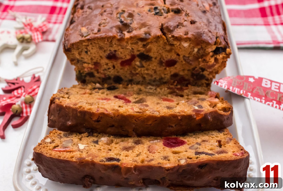 Closeup on a loaf of The Best Fruit Cake, perfectly ripened and displayed on a white serving platter, surrounded by festive Christmas decorations.