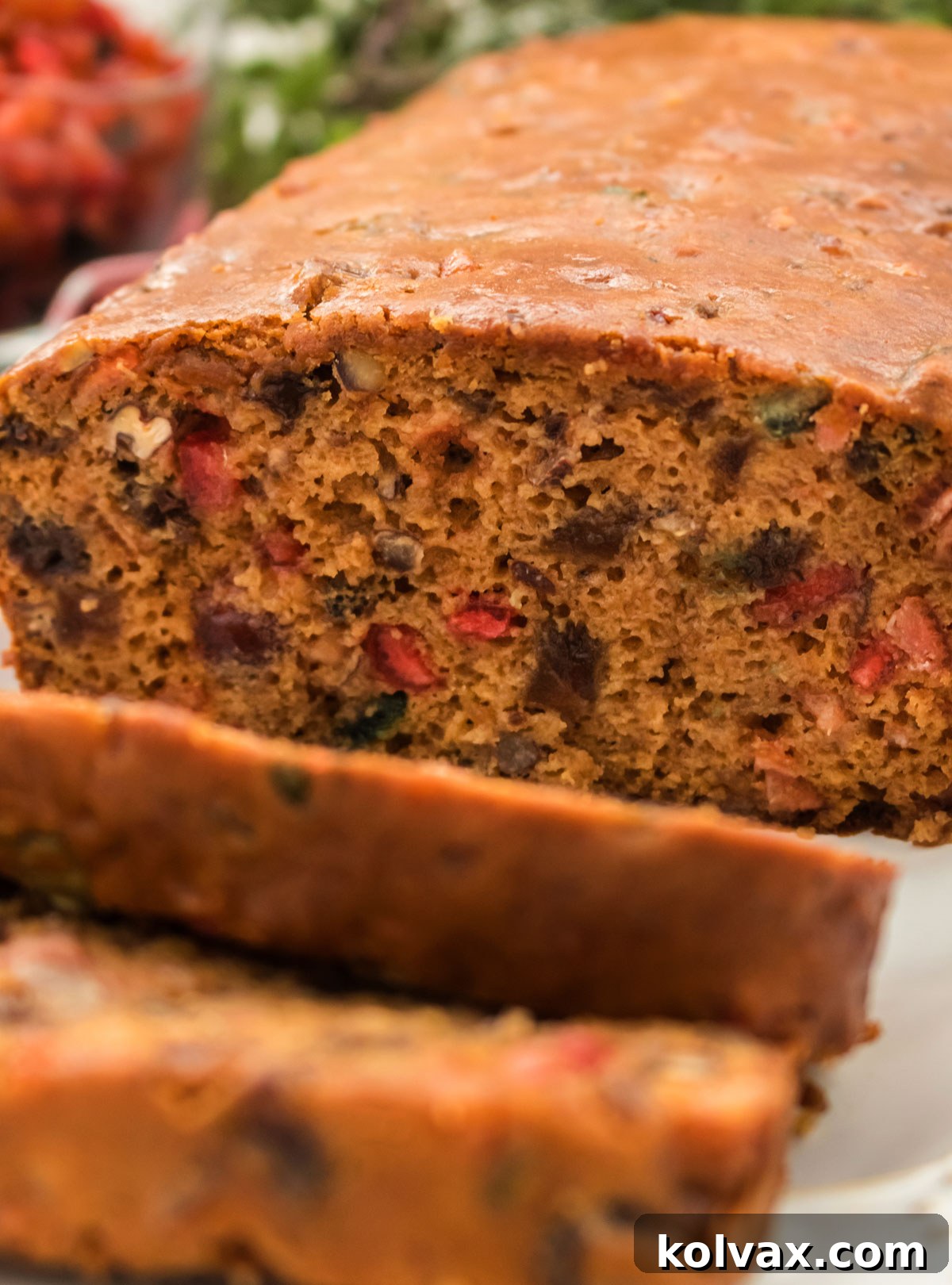 Closeup on a perfectly sliced loaf of The Best Fruit Cake on a white serving platter, showcasing its dense texture and rich fruit content.