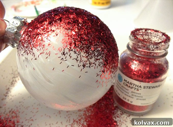 Generously sprinkle red glitter over the Mod Podge-covered Christmas ornament, ensuring complete coverage and allowing excess glitter to fall onto a tray.