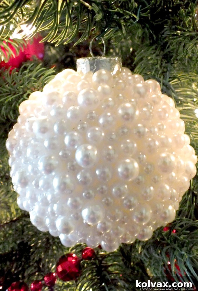 Close-up of a clear glass ornament being decorated with faux pearls using tacky glue, demonstrating the simple crafting technique.