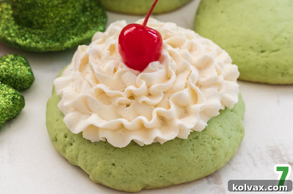 A beautifully frosted Shamrock Shake Mint Cookie with a generous swirl of Whipped Vanilla Frosting, perfectly crowned with a bright red Maraschino Cherry, presented against a clean background.