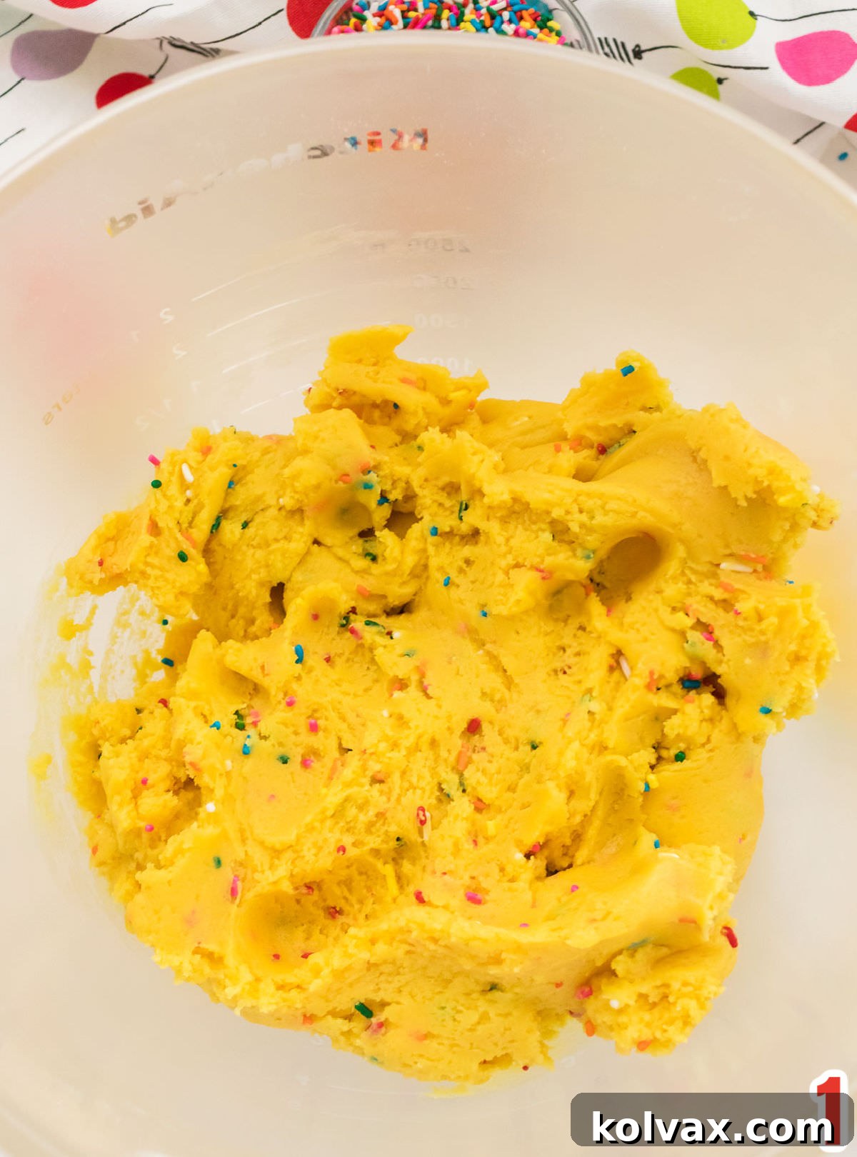 A clear glass mixing bowl holds a perfectly blended, colorful batch of Cake Mix Cookie dough, flecked with bright sprinkles.