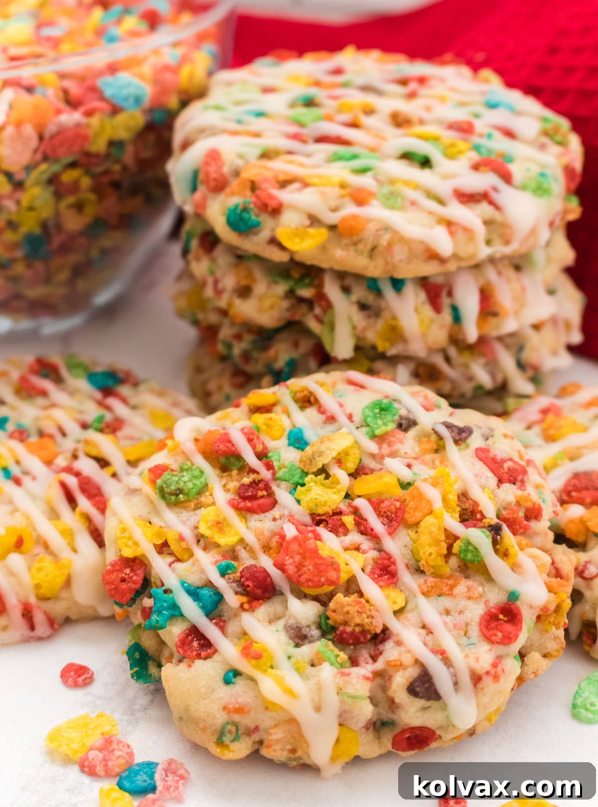Closeup on a Fruity Pebbles Sugar Cookie propped up against another stack of cookies and in front of a glass bowl filled with. Fruity Pebbles Cereal.