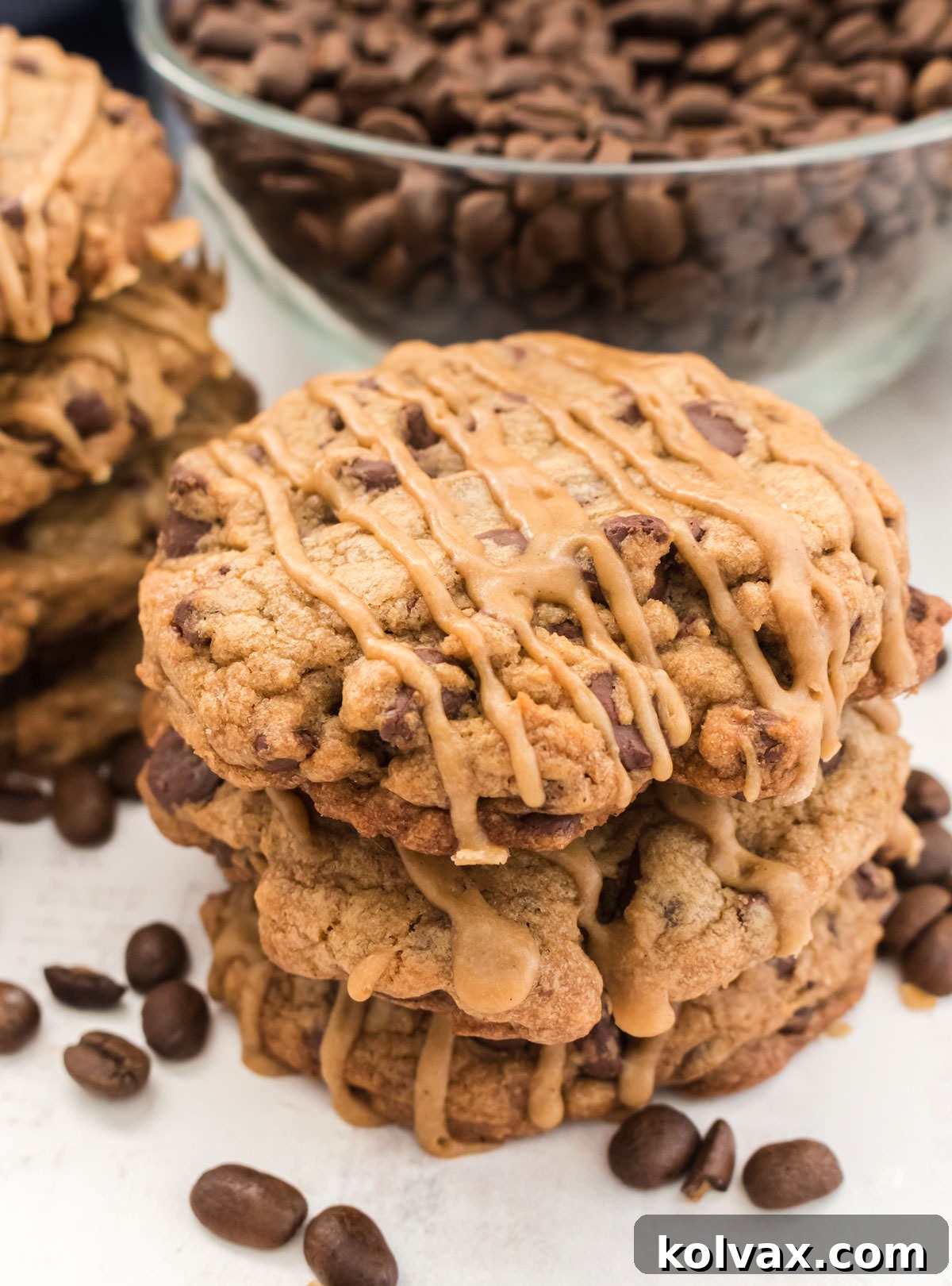 A beautiful close-up of a stack of three Coffee Chocolate Chip Cookies, glistening with coffee icing, set against a backdrop of more cookies and a glass bowl filled with fragrant coffee beans, inviting viewers to indulge.