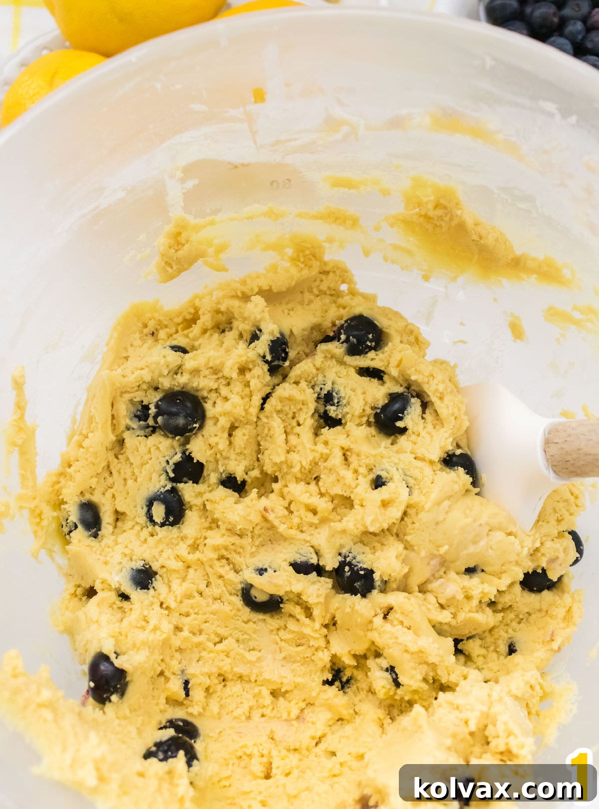 Closeup on a glass mixing bowl filled with vibrant Lemon Blueberry cookie dough and a white wooden spatula, showcasing the perfectly incorporated ingredients.
