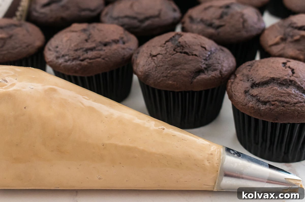 Velvet Coffee Buttercream 7 A piping bag filled with creamy Coffee Buttercream Frosting rests beside a tray of unfrosted chocolate cupcakes, ready for decoration.