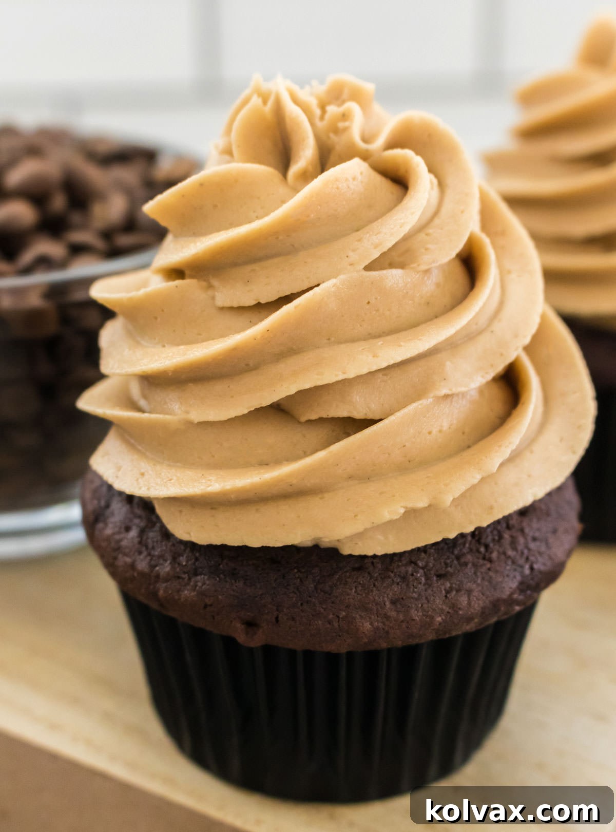 Velvet Coffee Buttercream 8 A close-up shot of a single chocolate cupcake, beautifully topped with a generous swirl of The Best Coffee Frosting, sitting in front of a glass bowl filled with roasted coffee beans.