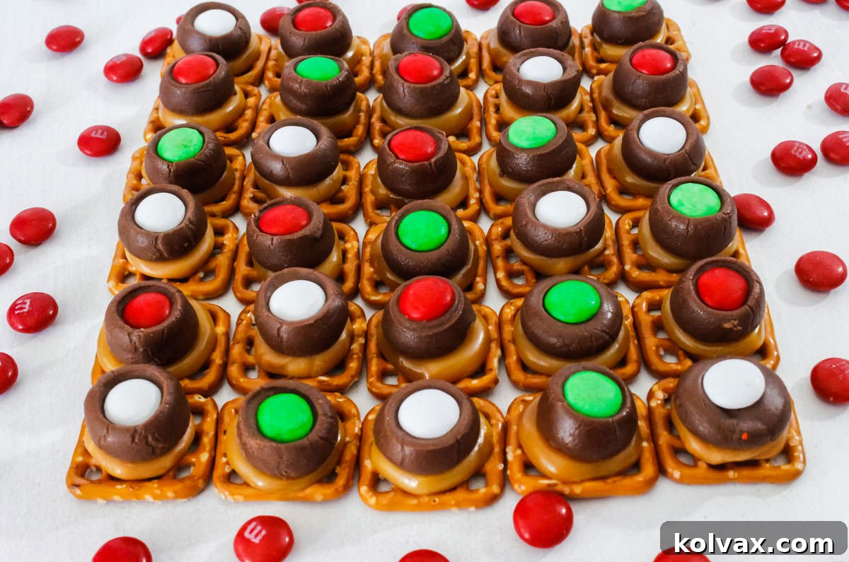 Closeup on a batch of festive Christmas Caramel Pretzel Bites arranged in neat rows on a white surface, showcasing their vibrant red and green M&M toppings and gooey caramel.