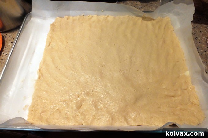 Pressing down the Frozen Sugar Cookie dough evenly across the cookie sheet using buttered hands.