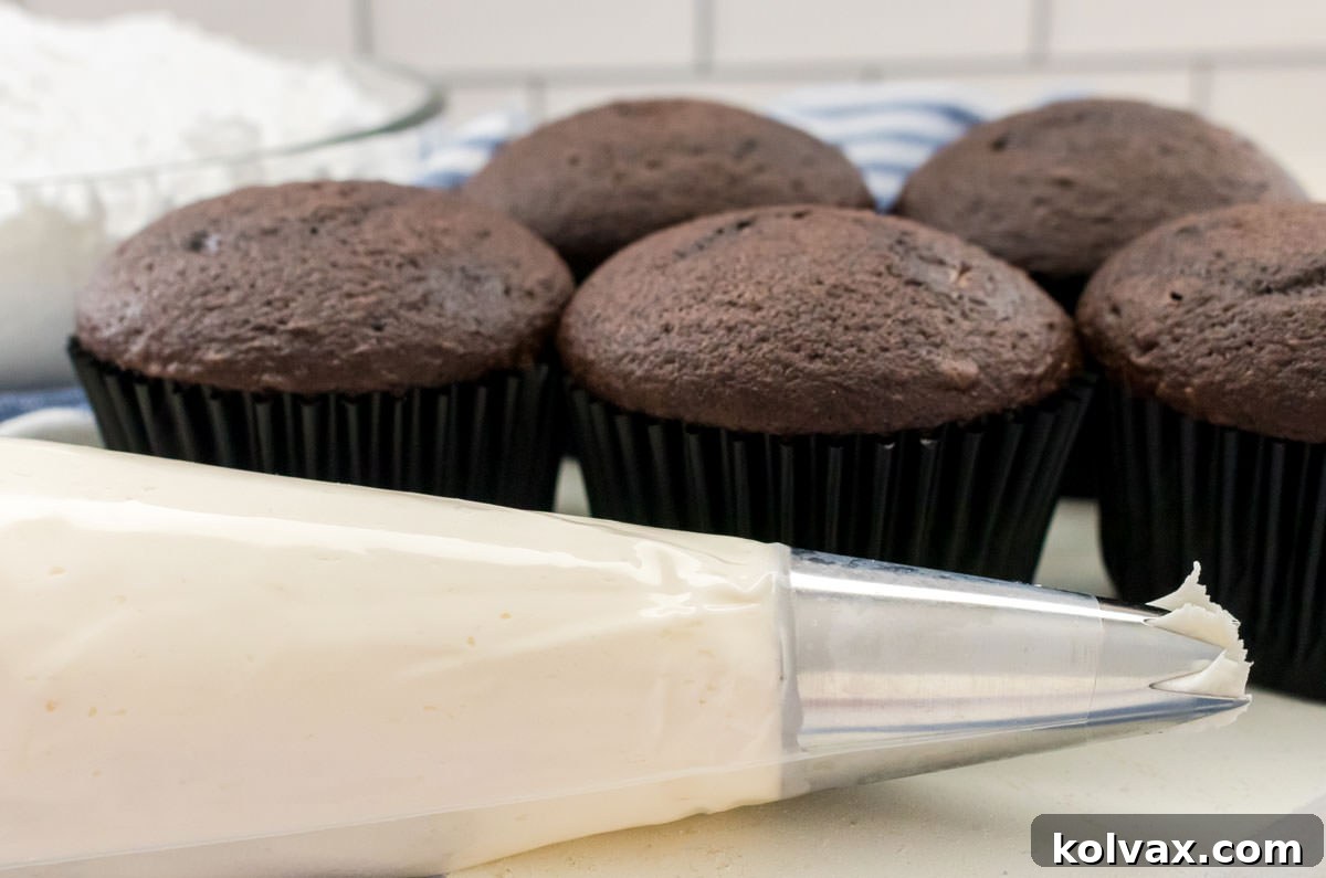 Closeup on a decorating bag filled with Whipped Vanilla Buttercream Frosting sitting in front of a batch of unfrosted chocolate cupcakes.