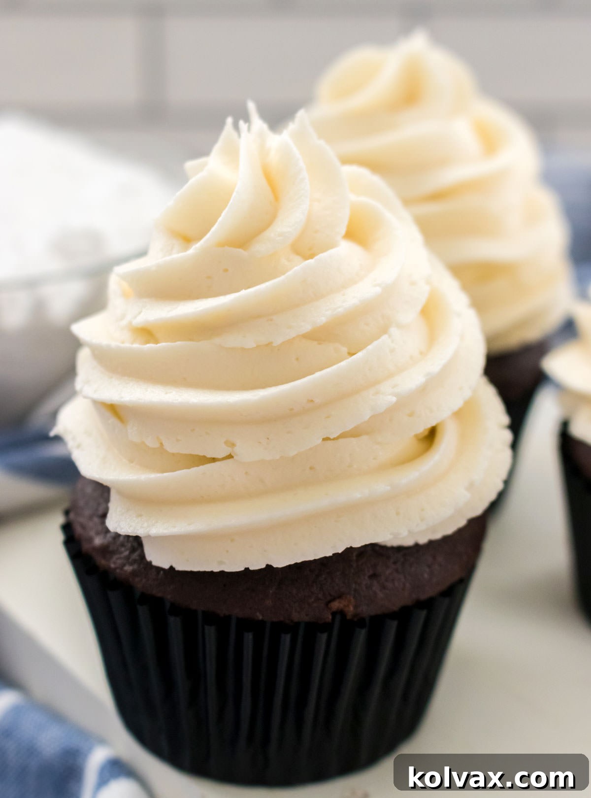 Closeup on two cupcakes topped with The Best Whipped Vanilla Frosting sitting next to a bowl of powdered sugar.