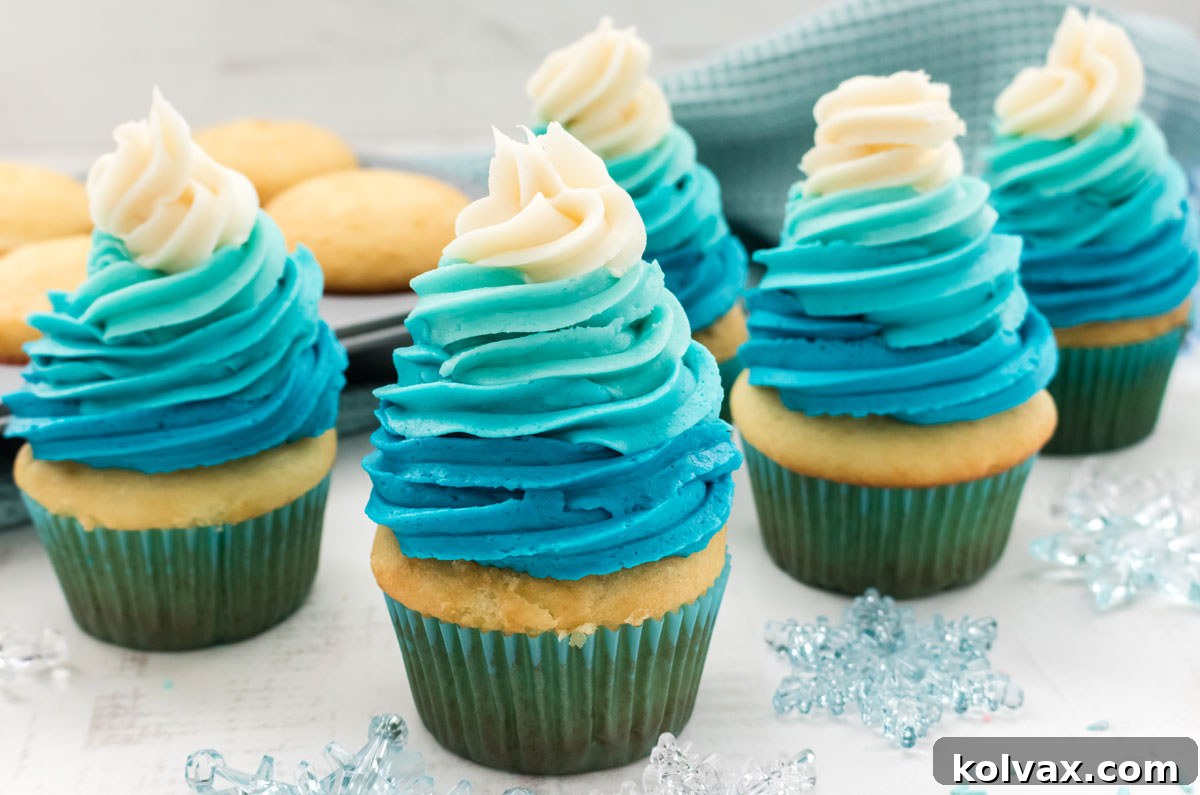 Crystalline Gradient Swirl Cupcakes 2 Closeup on five Frozen Ombre Swirl Cupcakes sitting on a white table surrounded by snowflake decorations, cupcakes and a blue table linen. Perfect for a Frozen-themed birthday party.