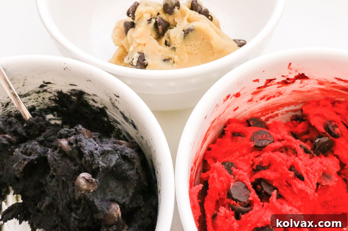 Three white bowls filled with black, red and white chocolate chip cookie dough.