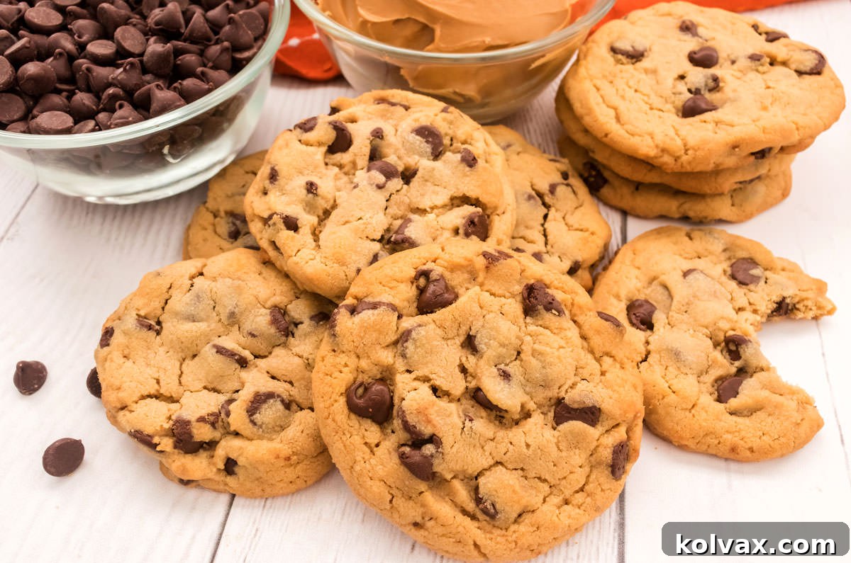 Closeup on a batch of Peanut Butter Chocolate Chip Cookies laying on a white table in front of ramekins filled with chocolate chips and peanut butter.