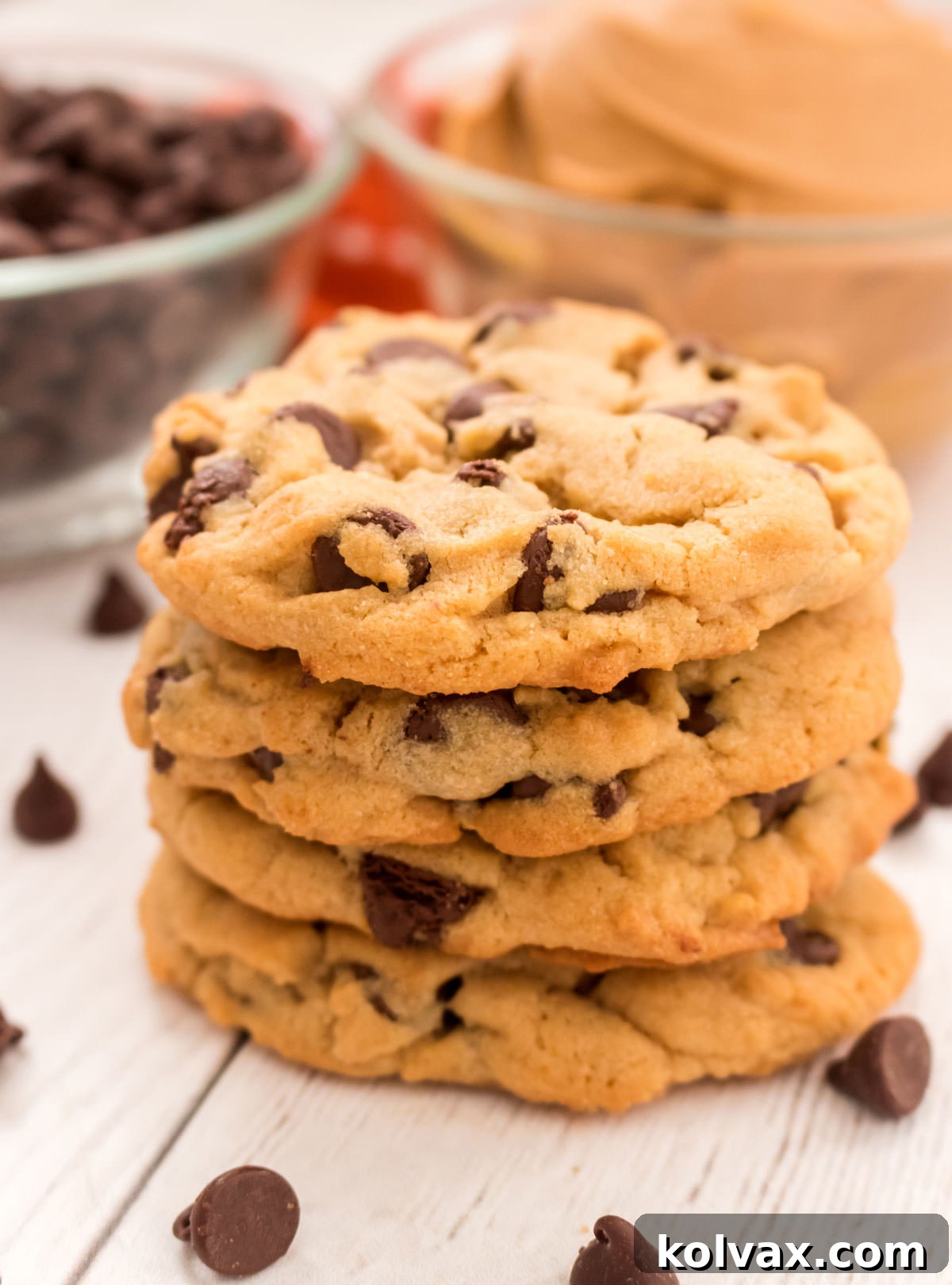 Closeup on a stack of Peanut Butter Chocolate Chip Cookies sitting on a white table in front of glass bowls filled with peanut butter and chocolate chips.