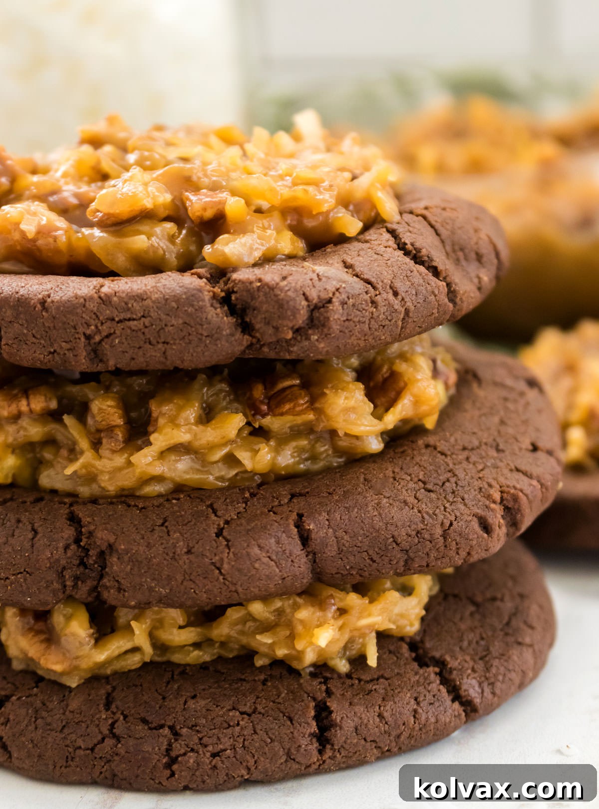 Closeup of a neat stack of German Chocolate Cookies, each perfectly frosted, sitting on a white table.