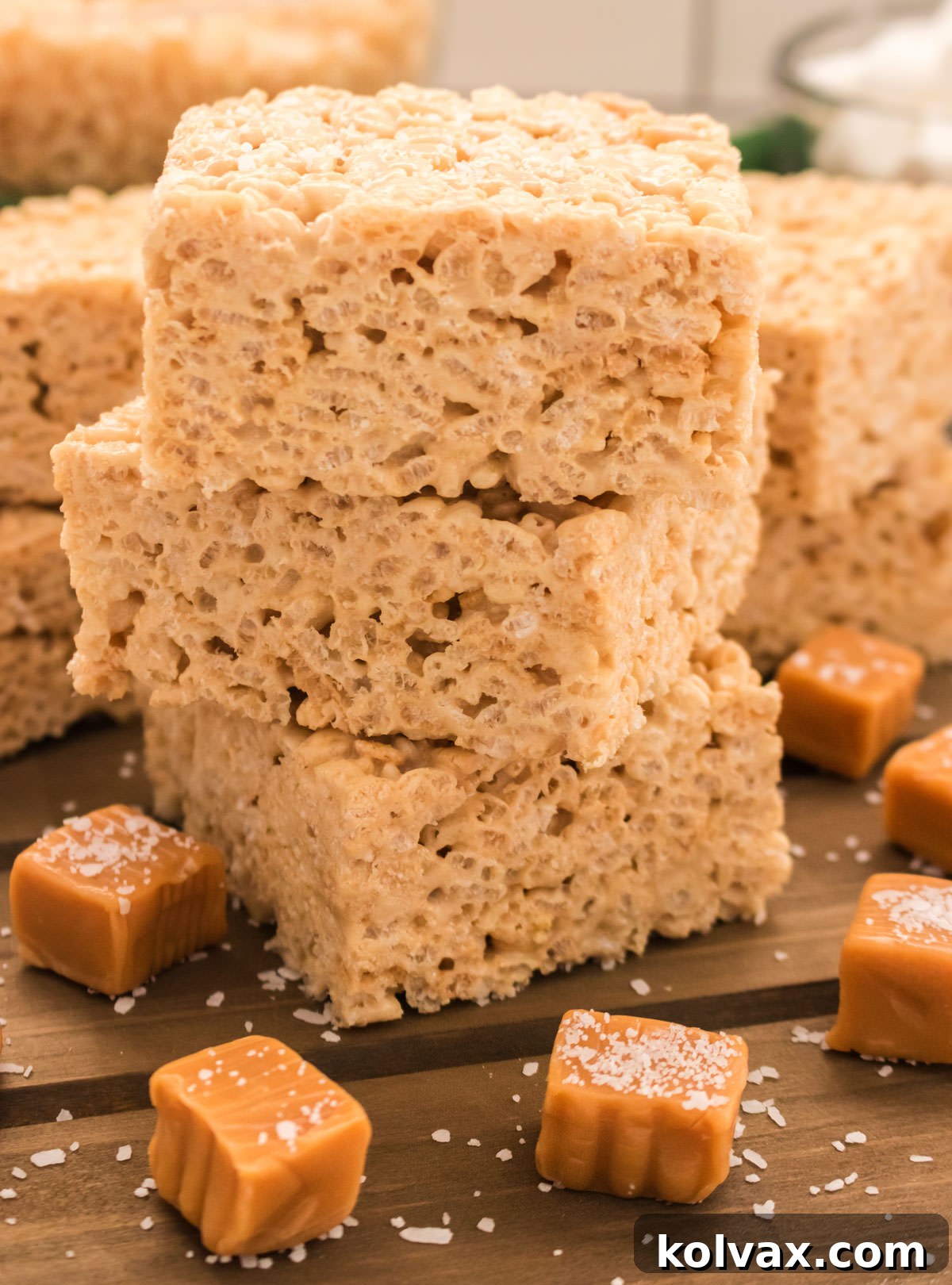 Salted Caramel Krispie Bliss 8 A close-up of a stack of two freshly cut Salted Caramel Rice Krispie Treats on a cutting board, garnished with loose caramel candies and a sprinkle of flaky sea salt, highlighting their golden, gooey texture and perfect crispness. The edges are clean and inviting.