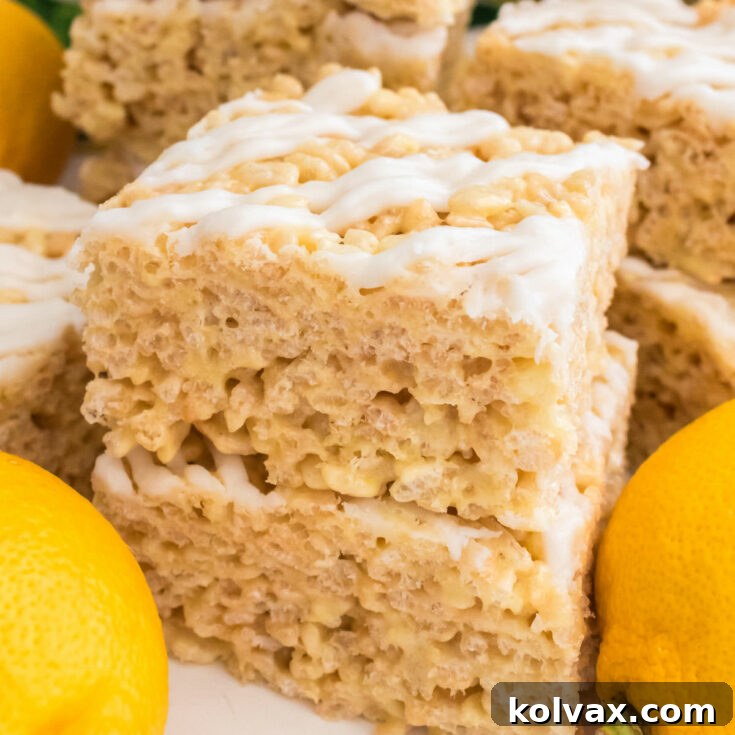 Picture of two bright yellow Lemon Rice Krispie Treats sitting on a white table surrounded by fresh lemons and ingredients, ready to be enjoyed.