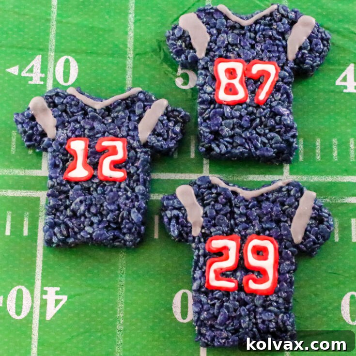 Three New England Patriots Rice Krispie Treats laying on a table covered with a Football table cloth.