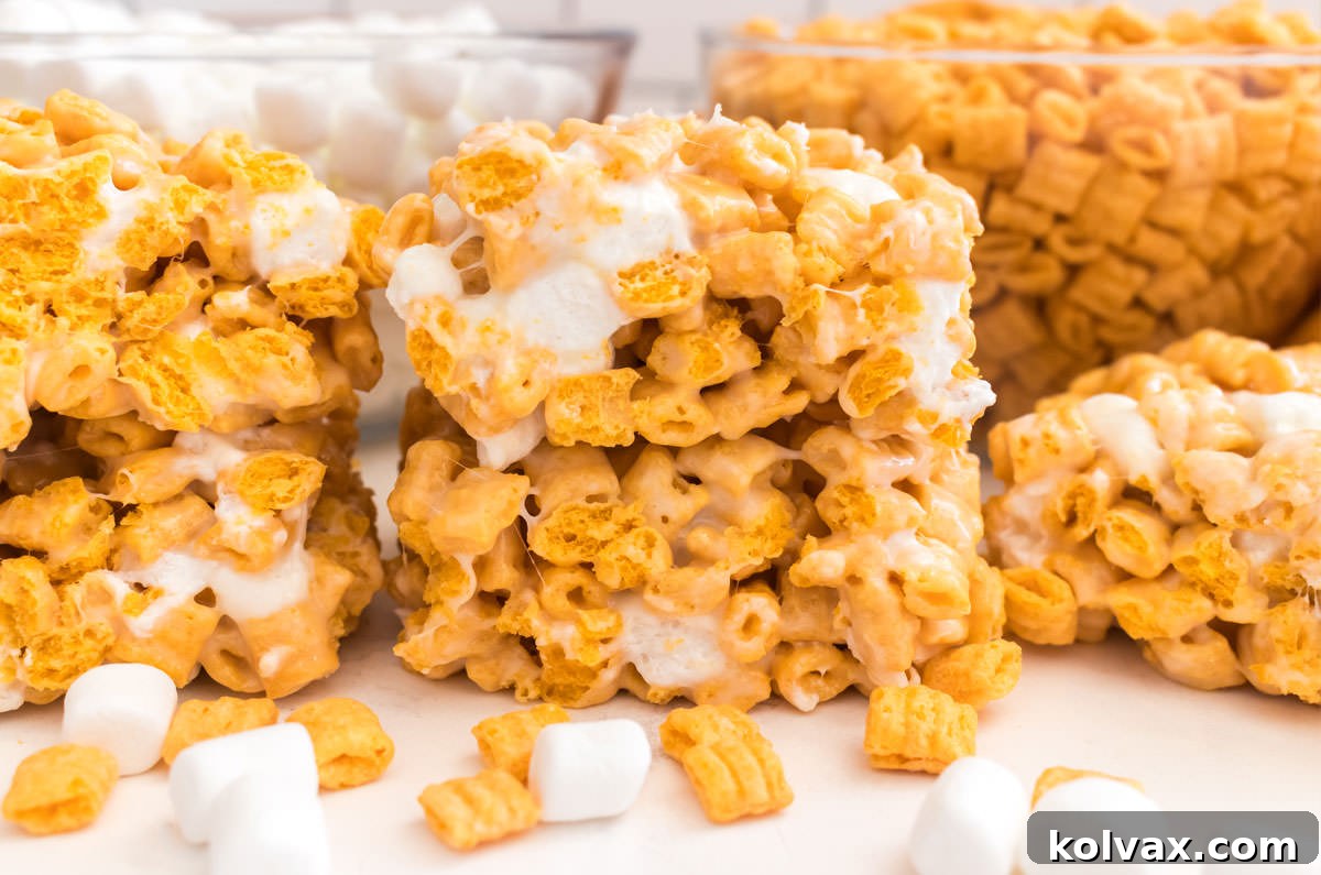 A vibrant batch of golden Cap'n Crunch Marshmallow Treats, freshly made and ready to enjoy, sits on a pristine white table. In the background, inviting bowls of colorful Cap'n Crunch cereal and fluffy mini marshmallows hint at the delicious ingredients used.