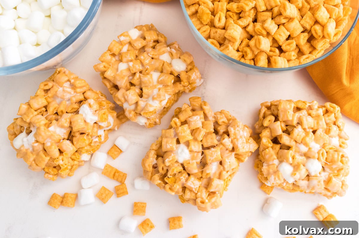 Four perfectly cut Cap'n Crunch Marshmallow Treats arranged on a white table, surrounded by loose Cap'n Crunch Cereal and a scattering of mini marshmallows, showcasing their inviting texture.
