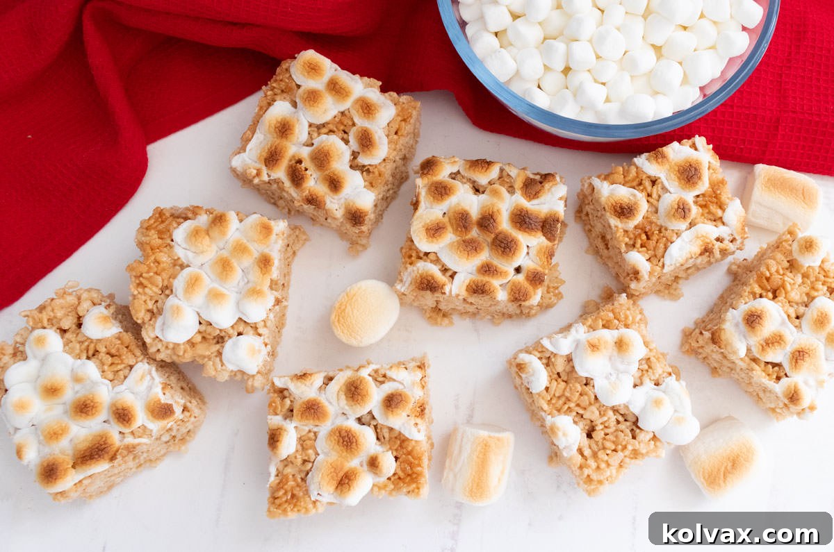 An overhead shot showcasing a perfectly arranged batch of eight Toasted Marshmallow Rice Krispie Treats on a clean white table, accompanied by a festive red kitchen towel.