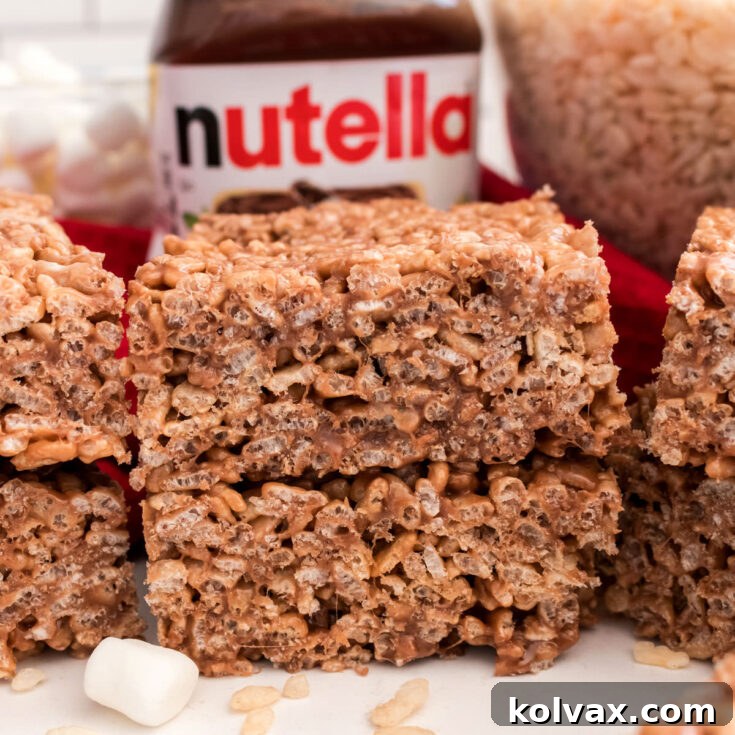 A batch of Nutella Rice Krispie Treats sitting on a white table alongside a jar of Nutella spread.