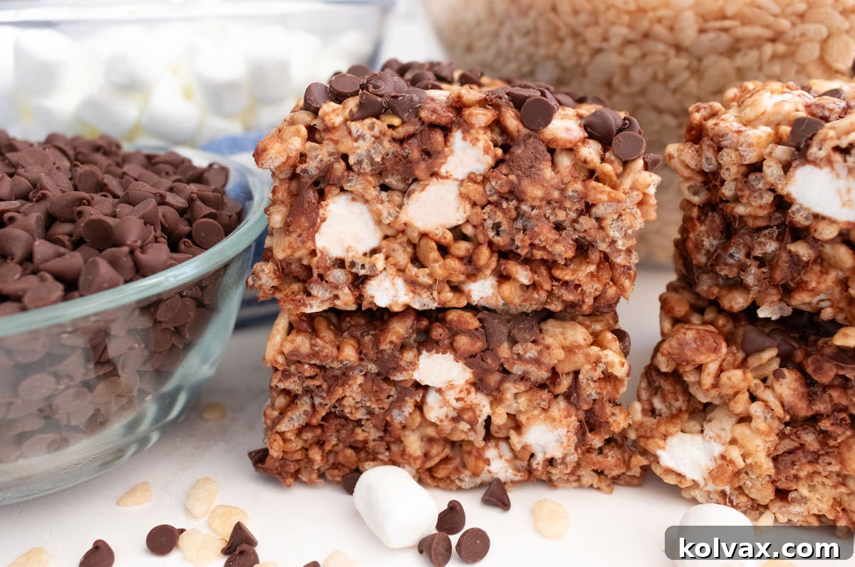 A stack of two beautifully textured Zebra Rice Krispie Treats, showcasing the melted marshmallow and visible mini chocolate chips, presented on a clean white table beside a clear glass bowl brimming with mini chocolate chips.