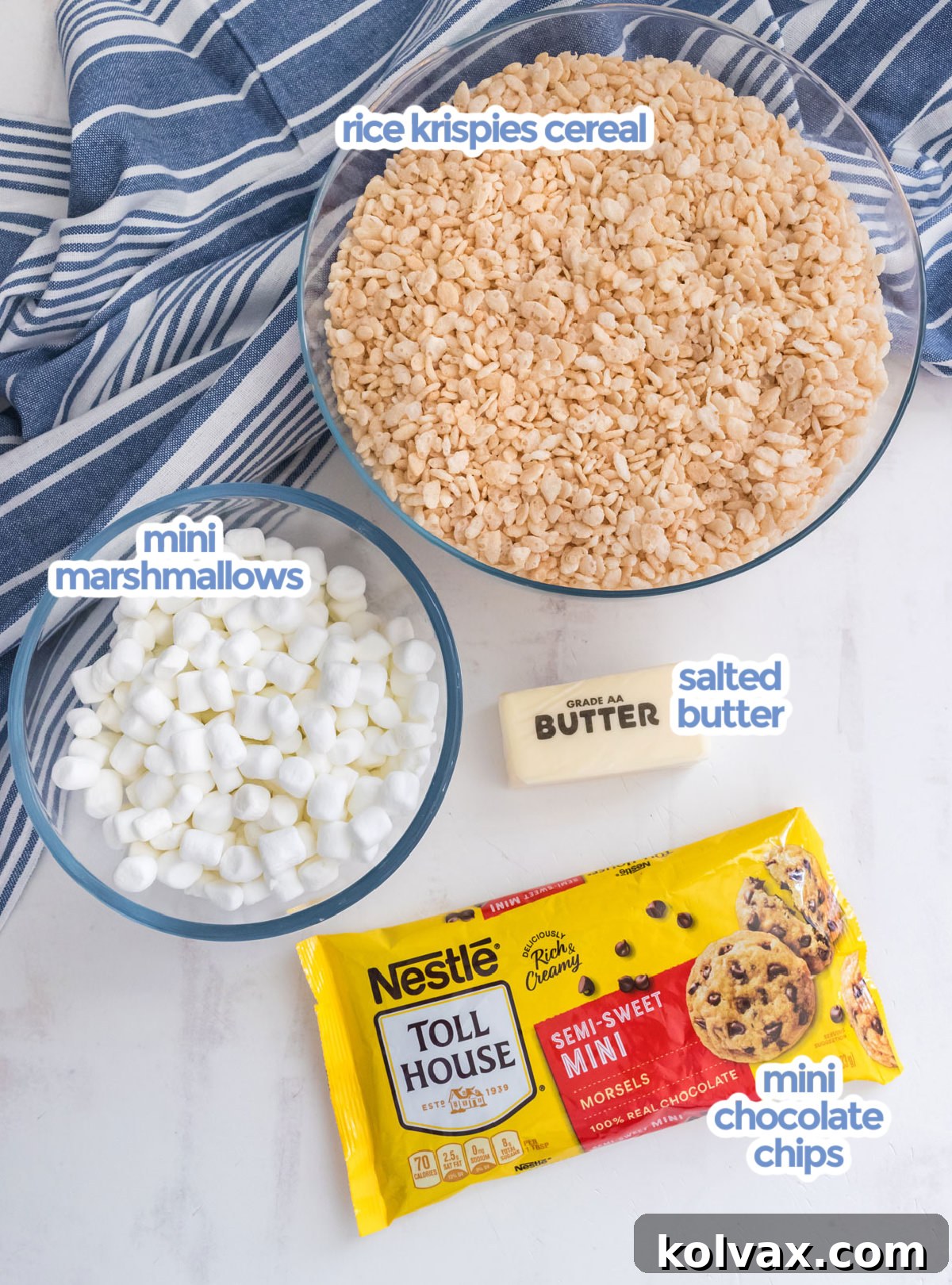 All the essential ingredients neatly arranged for making Zebra Rice Krispie Treats: a stick of butter, a bag of mini marshmallows, a box of Rice Krispies cereal, and a bowl of mini chocolate chips.