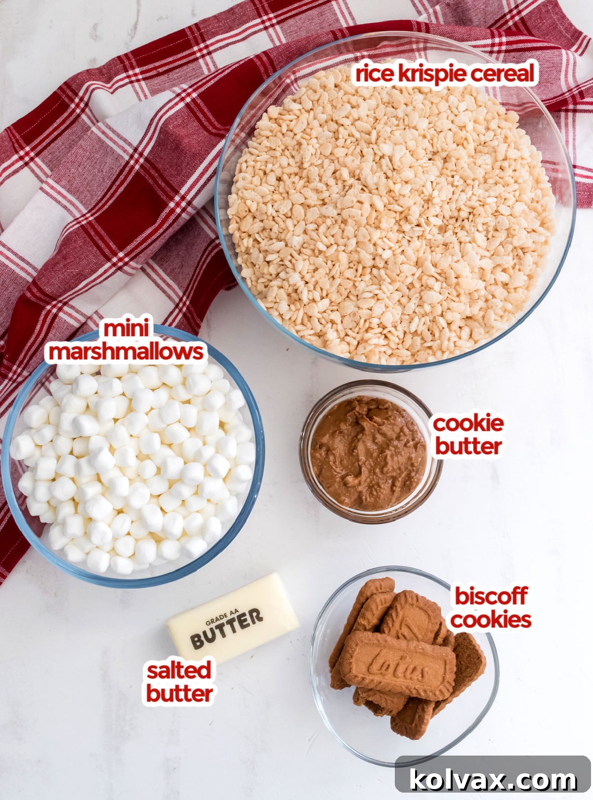 All the essential ingredients for making Cookie Butter Rice Krispie Treats laid out on a white surface, including butter, marshmallows, cookie butter, Rice Krispies cereal, and Biscoff cookies.