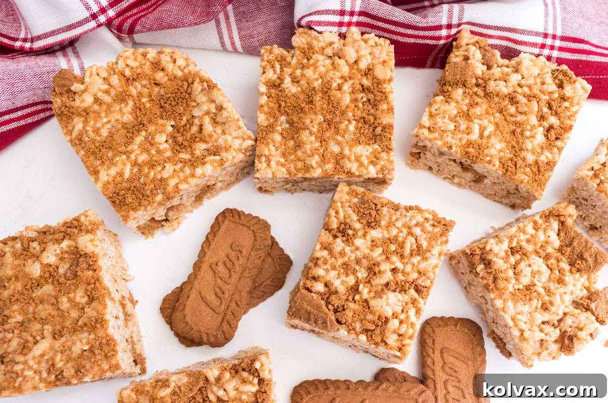 An overhead shot of a freshly made batch of Cookie Butter Rice Krispie Treats resting on a pristine white table, alongside a rustic red kitchen towel.
