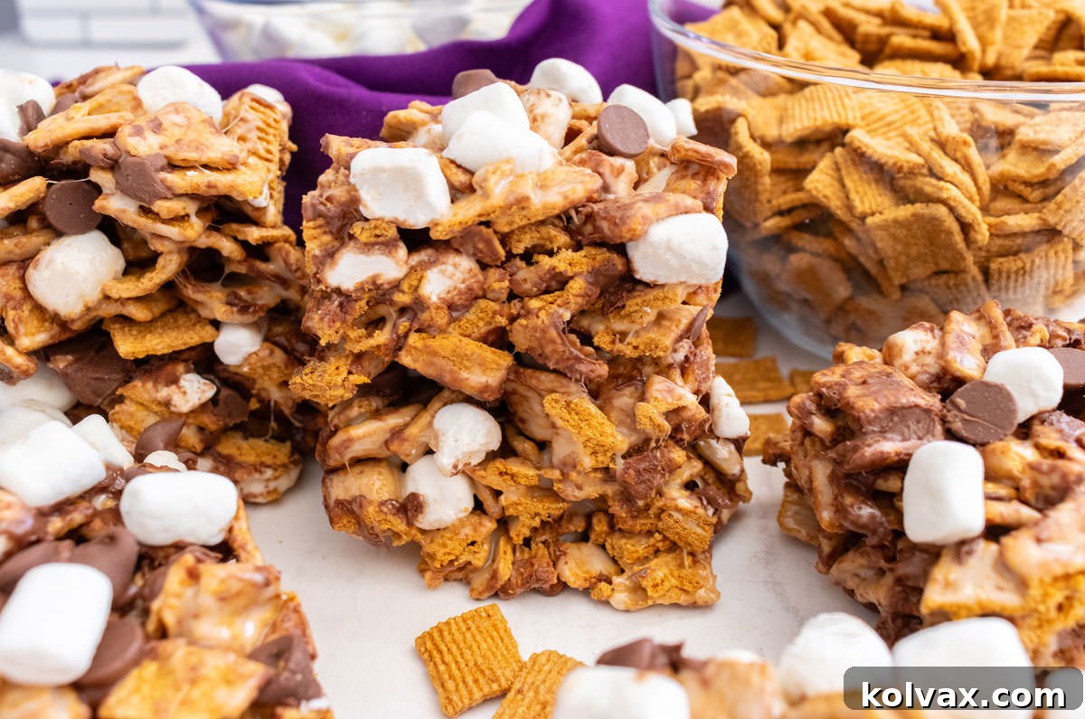 Six Golden Grahams S'mores Marshmallow Treats neatly arranged on a white table. In the background, glass bowls hold Golden Grahams cereal and mini marshmallows, setting a delicious scene.