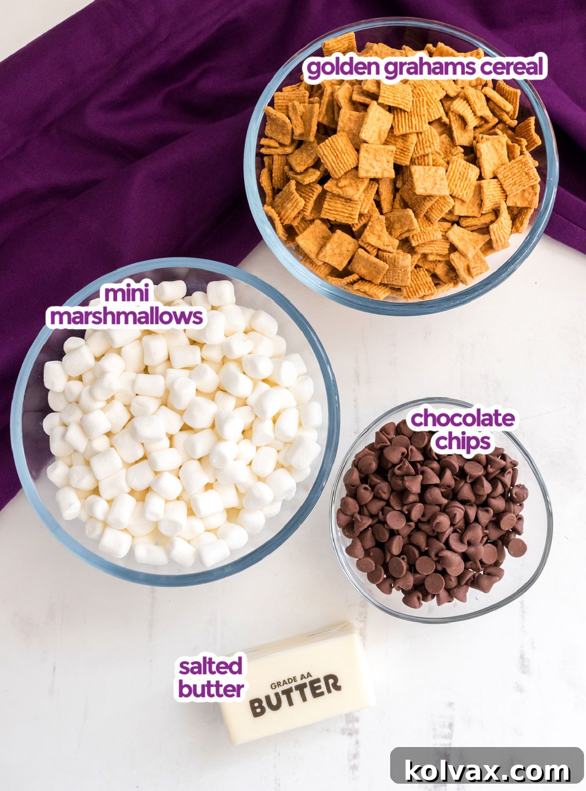All the essential ingredients neatly laid out on a white surface for making Golden Grahams S'mores Marshmallow Treats, including butter, mini marshmallows, Golden Grahams cereal, and chocolate chips.